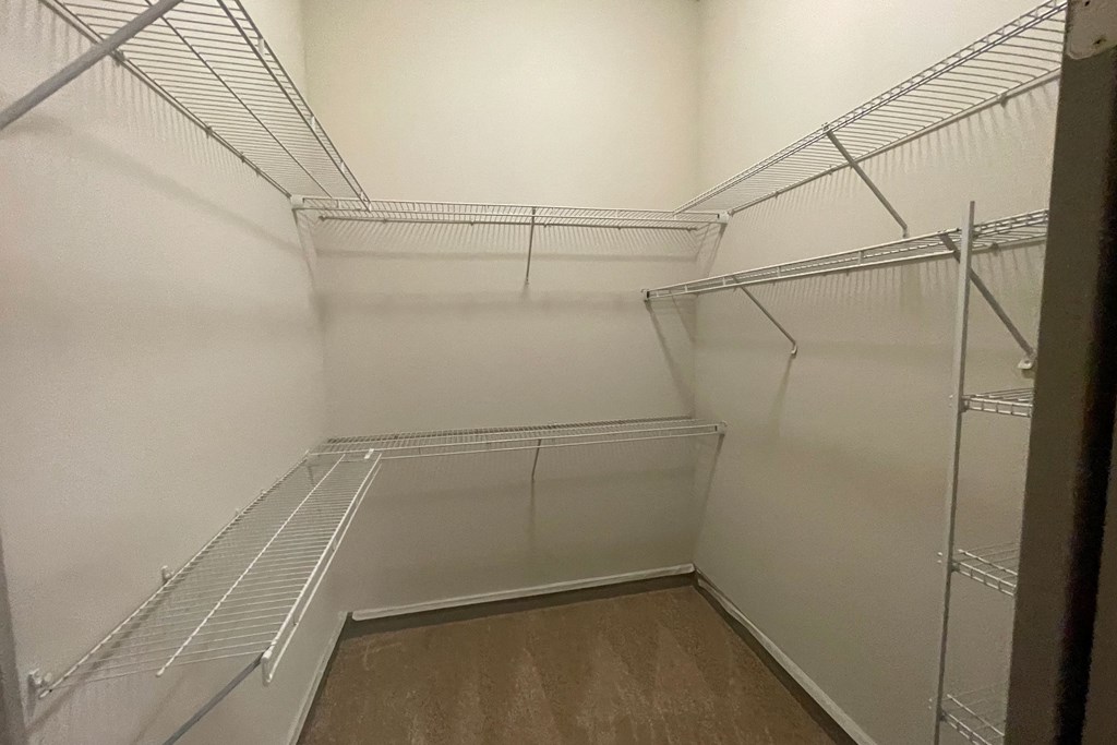 Empty walk-in closet here at Cityplace Heights Apartment Homes with beige carpet and white walls, featuring multiple white metal wire shelves and hanging rods on three sides.