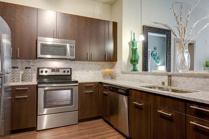 Modern kitchen here at Cityplace Heights Apartment Homes with dark wood cabinets, stainless steel appliances, and marble countertops. Green vase and decorative mirror add elegant accents. Cozy ambiance.