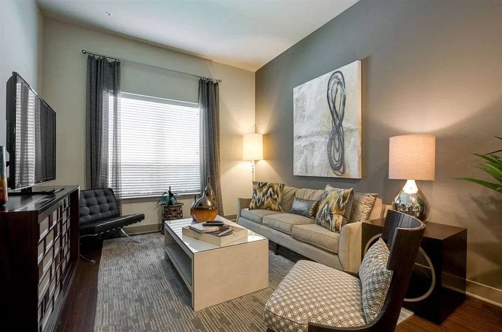 Modern living room here at Cityplace Heights Apartment Homes with gray walls, beige sofa adorned with patterned cushions, and sleek furniture. Abstract art and soft lighting create a cozy atmosphere.