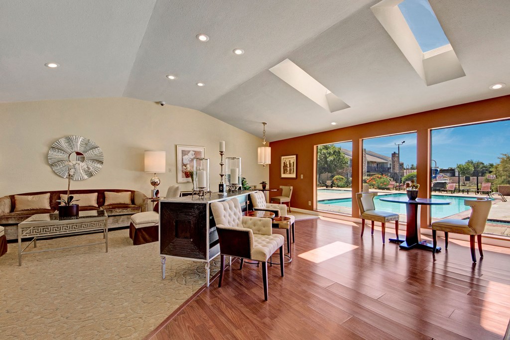 Elegant resident lounge here at Cypress Pointe Apartment Homes with large windows, wood floors, modern furniture, and pool view. Skylights add natural light, creating a serene, inviting atmosphere.