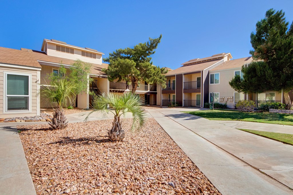 Sunny courtyard of Fairgreen Apartment Homes with balconies, surrounded by trees and gravel landscaping, under a clear blue sky. Peaceful atmosphere.