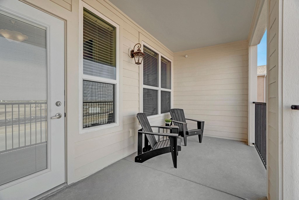 A small balcony here at Latitude 31 Apartment Homes with a beige chair and a potted plant on a table overlooks a vast, flat landscape under a clear blue sky, conveying calmness and openness.