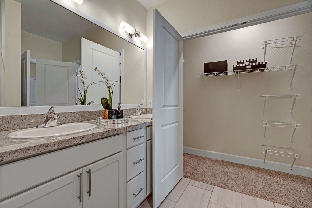 Spacious bathroom with a granite countertop and sink. A large mirror reflects a storage closet, creating a clean, modern look.