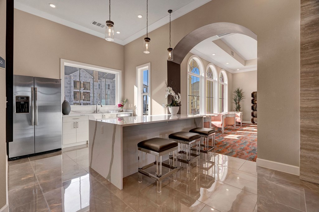 Modern Resident Lounge here at Latitude 31 Apartment Homes with a marble island, three leather stools, and large windows. Adjacent living room visible through an archway, creating a welcoming atmosphere.