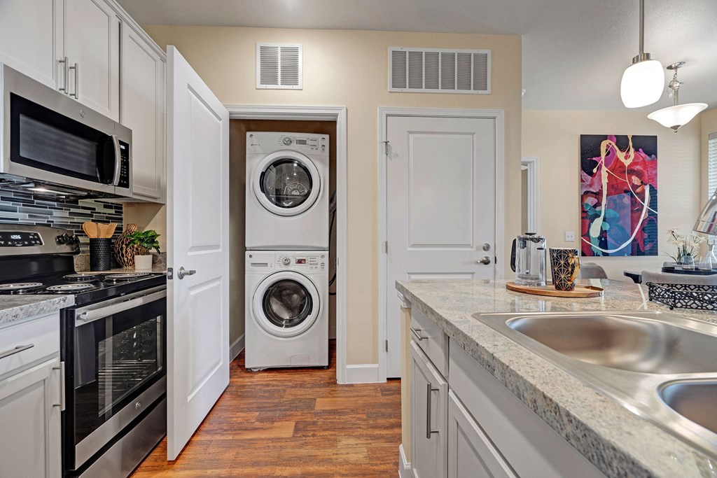 Modern kitchen here at Latitude 31 Apartment Homes with granite countertop island, pendant lights, and hardwood floor. Open layout includes dining area and seating, creating a bright, welcoming space.