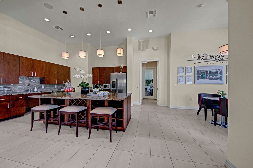Spacious kitchen here at Le Mirage Apartment Homes with modern design, featuring a large island, bar stools, pendant lights, and stainless steel appliances. Mood is welcoming and elegant.