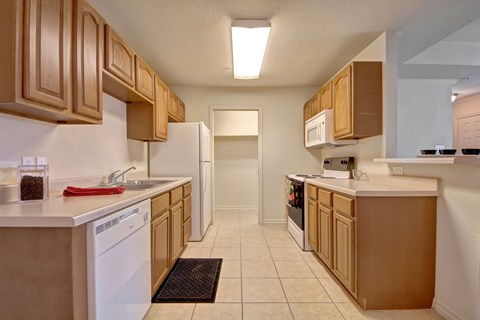 A well-lit kitchen here at Lexington Court Apartment Homes with tan wooden cabinets and beige countertops. It features a refrigerator, stove, microwave, dishwasher, and cream tile floor. The space looks clean and inviting.