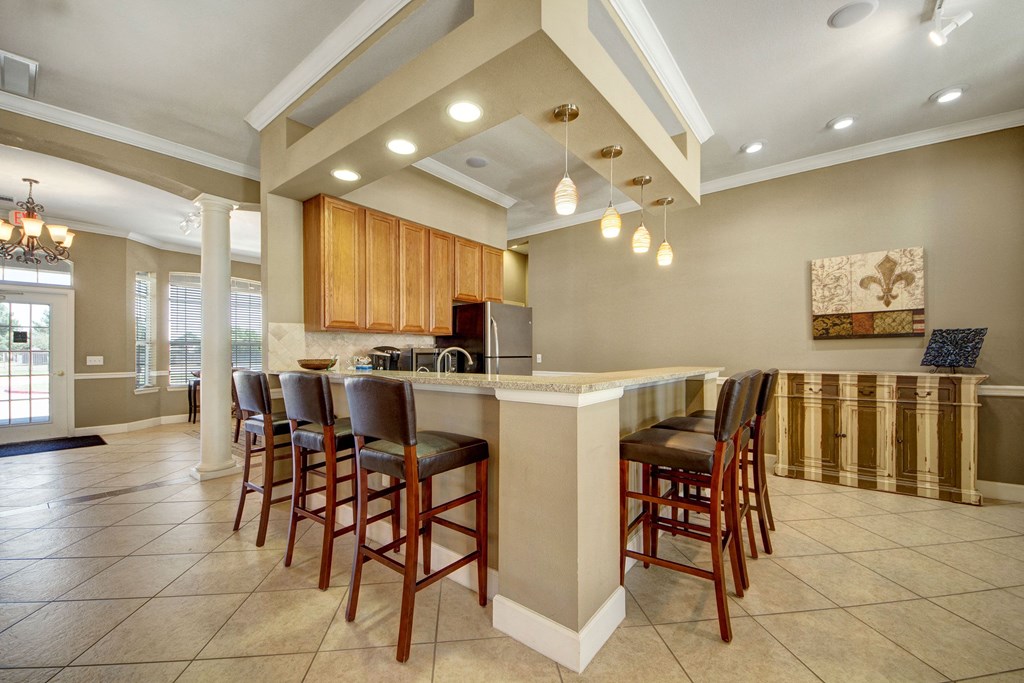 Spacious kitchen here at Mission Green Apartment Homes with a large island and bar stools, pendant lights hang from the ceiling. Warm tones and tile flooring create an inviting atmosphere.