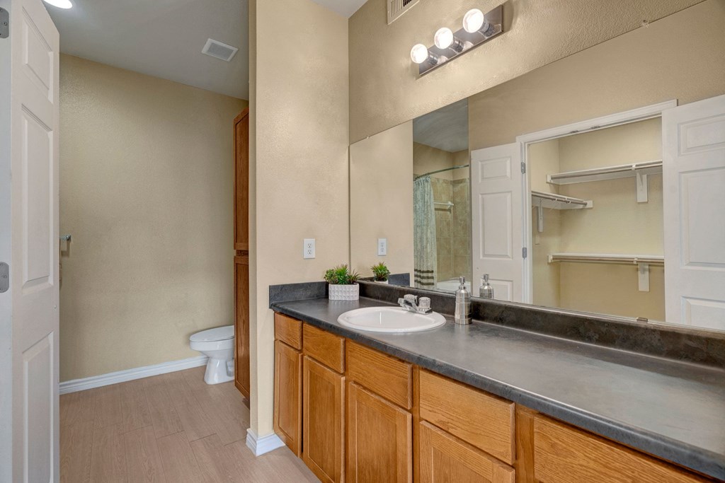 Empty beige walk-in closet here at Mission Green Apartment Homes with open door, wooden rods, and shelves. The room appears clean and organized, conveying a sense of spaciousness.
