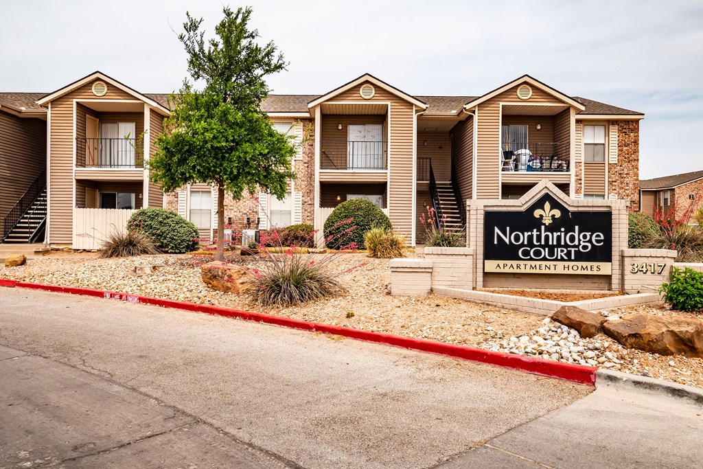 Front view of Northridge Court Apartment Homes, featuring a landscaped area with desert plants, a prominent sign, and a row of multi-level units.