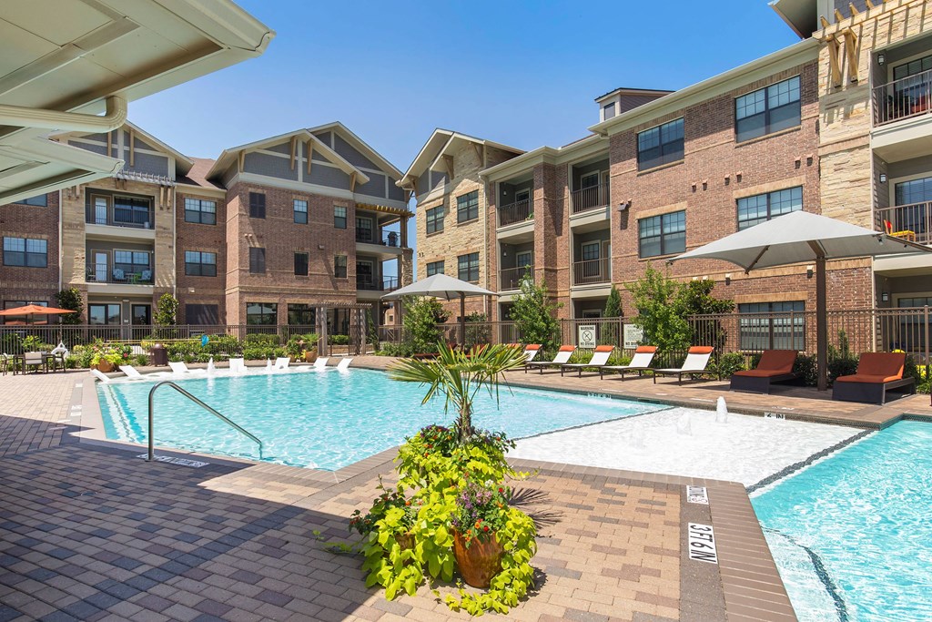 Spacious courtyard here at Sorrel Fairview Apartment Homes with a sparkling pool, surrounded by brick buildings. Lounge chairs with umbrellas offer a relaxing and inviting atmosphere.