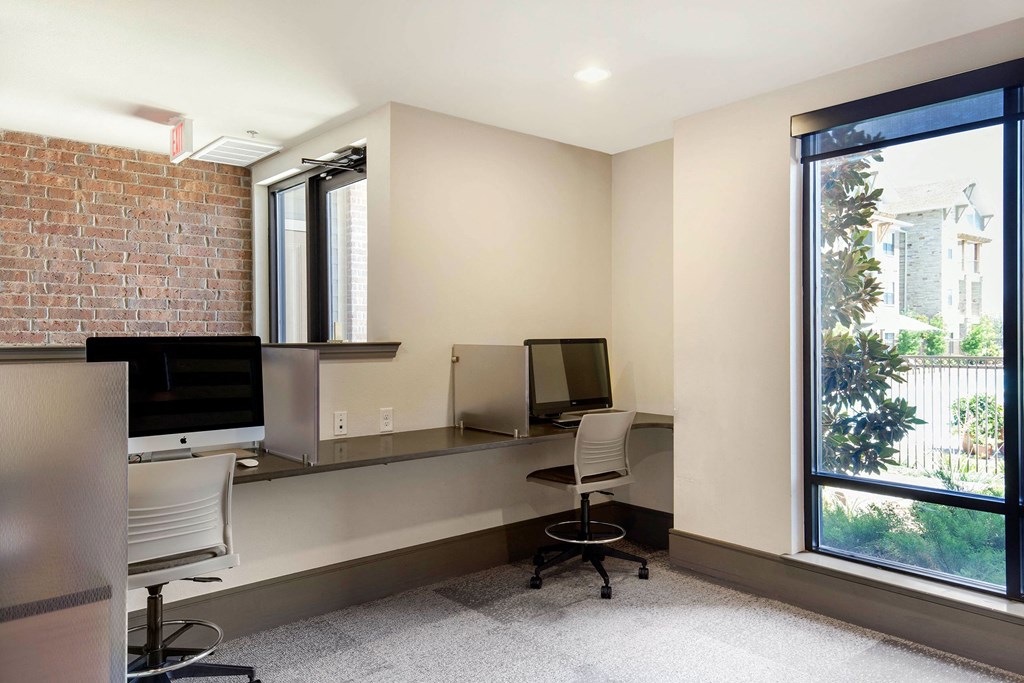 Modern office space here at Sorrel Fairview Apartment Homes with two computer workstations, swivel chairs, and large window. Bright, minimalist design with a calming, professional tone.