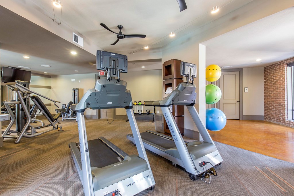 A modern gym here at Sorrel Fairview Apartment Homes with two sleek treadmills in the foreground, vibrant exercise balls stacked to the right, and strength machines in the background. Bright and inviting atmosphere.