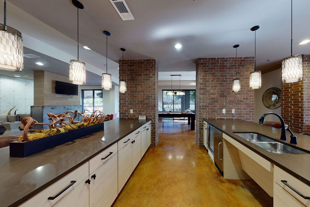 Spacious modern kitchen here at Sorrel Fairview Apartment Homes with brick walls, pendant lights, and dual countertops. Warm tones and sleek decor create a cozy, inviting atmosphere.