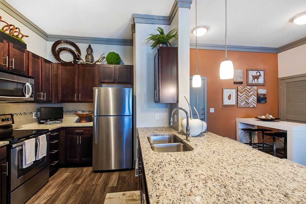 Modern kitchen here at Sorrel Fairview Apartment Homes with dark wood cabinets, stainless steel appliances, and granite countertops. Warm lighting and decorative accents create a welcoming atmosphere.