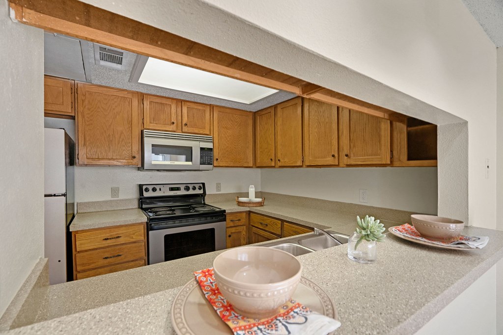 A cozy kitchen here at Summertree Place Apartment Homes with wooden cabinets, stainless steel appliances, and a light countertop. Two bowls on placemats add a warm, inviting touch.