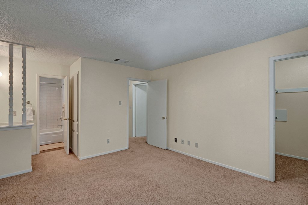 Empty room here at Summertree Place Apartment Homes with beige carpet and off-white walls, featuring an open door to a small bathroom with a shower. A closet and hallway are visible.