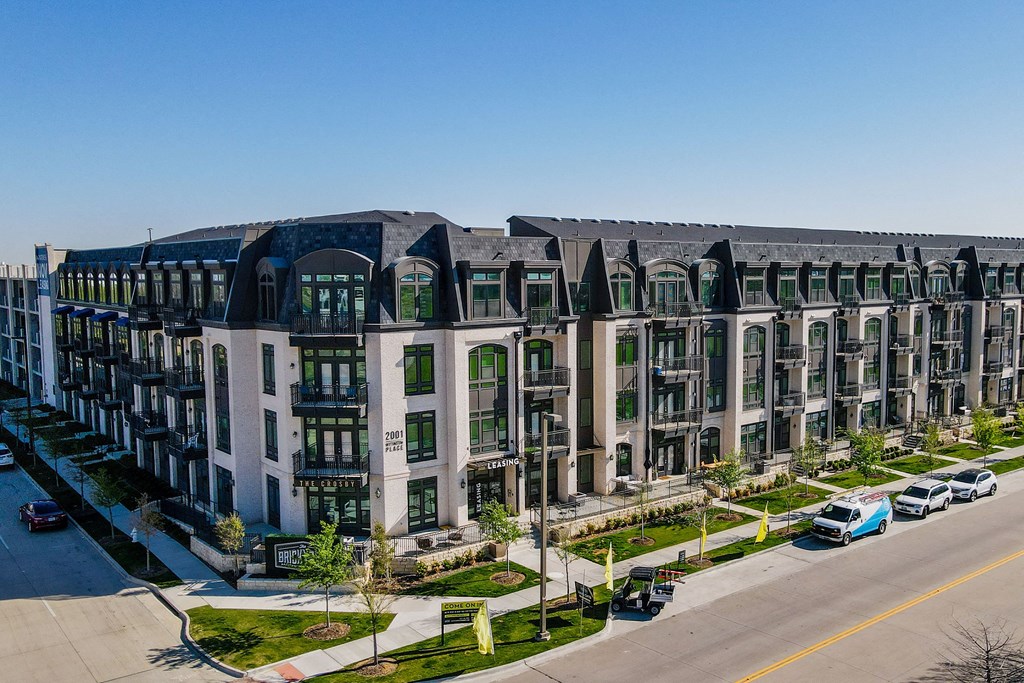 Urban The Crosby at The Brickyard Apartment Homes with a modern design, featuring four stories and arched windows. Lush landscaping and parked cars add to the vibrant scene.