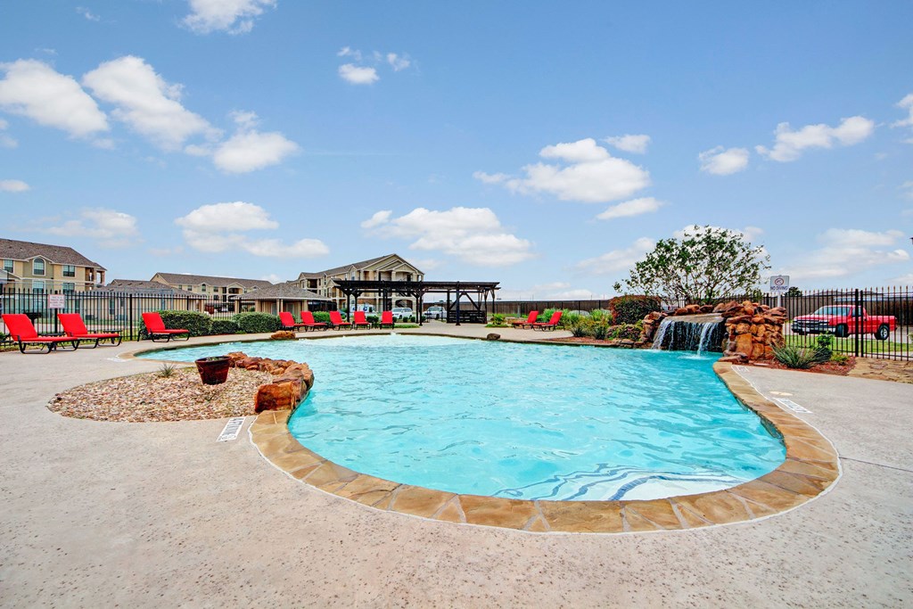 An outdoor pool for resident use surrounded by lounge chairs and a small waterfall Residence at Heritage Park Pool Apartments with a pool Abilene