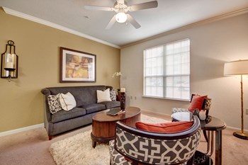 A cozy living room with a wide window overlooking the property and ceiling fan Residence at Heritage Park Living Room Abilene Texas Apartments for Rent - Photo Gallery 2