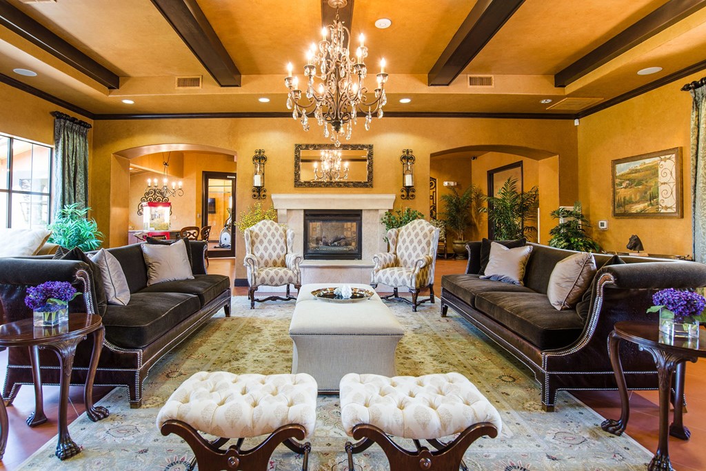 Luxurious living room here at Tuscany at Faudree Apartment Homes with elegant decor, featuring two velvet sofas, a fireplace, chandelier, and armchairs. Warm tones and plush furniture create an inviting ambiance.