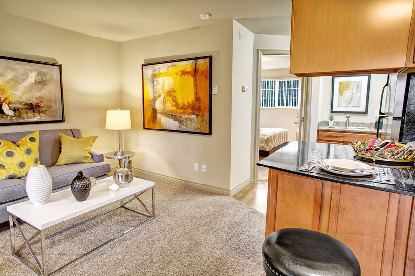 A living room with couch, coffee table, and view into the kitchen Colonial Square Living Room Apartments in Bellevue, WA