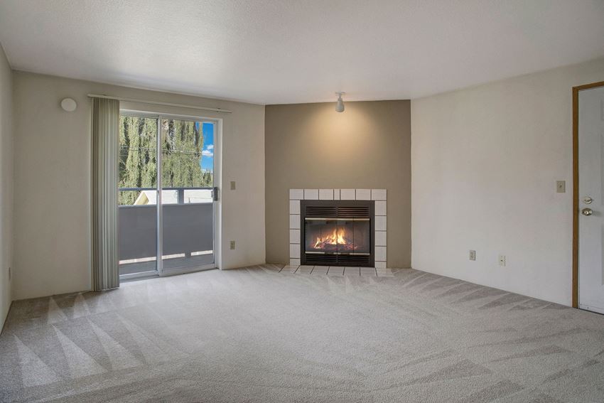 A cozy living room with a fireplace and sliding glass doors leading out to the balcony Glennbrook Living Room Apartments in Lynnwood, WA