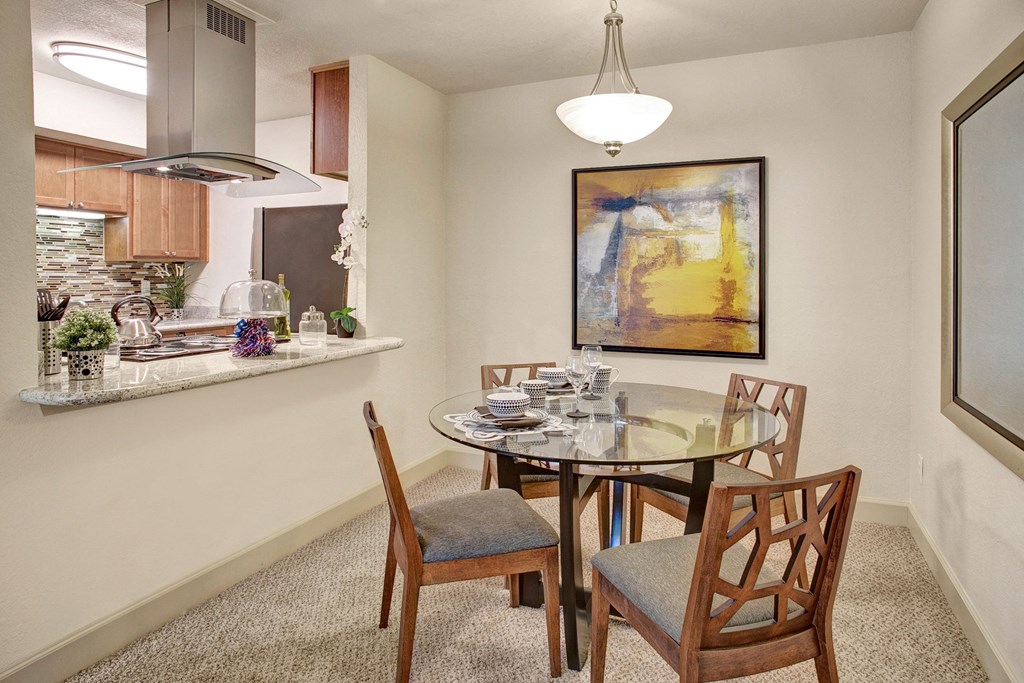 a dining area with a glass table and chairs and a kitchen in the background