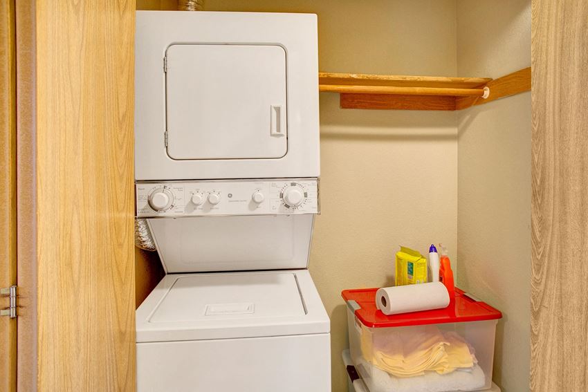 A stacked washer and dryer in a closet with shelving for storage Heron View Laundry Apartments in Kenmore, WA - Photo Gallery