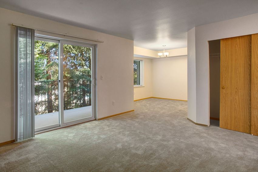 A spacious living room with sliding glass doors leading out to the balcony and a view into the dining area Lake Park Living Room Apartments in Everett, WA