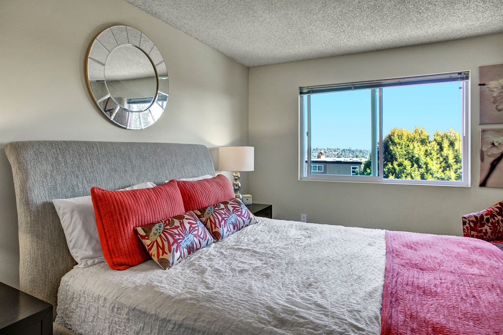 A bedroom with two nightstands and a bed with a large window overlooking the property Overlook at Magnolia Bedroom Apartments in Seattle, WA