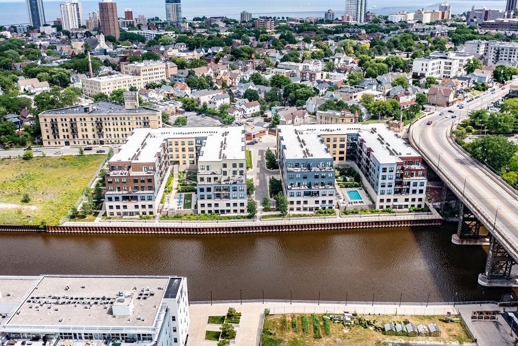 Aerial view of a cityscape featuring River House Apartments along a river. A nearby bridge crosses the water, with a dense urban area in the background.