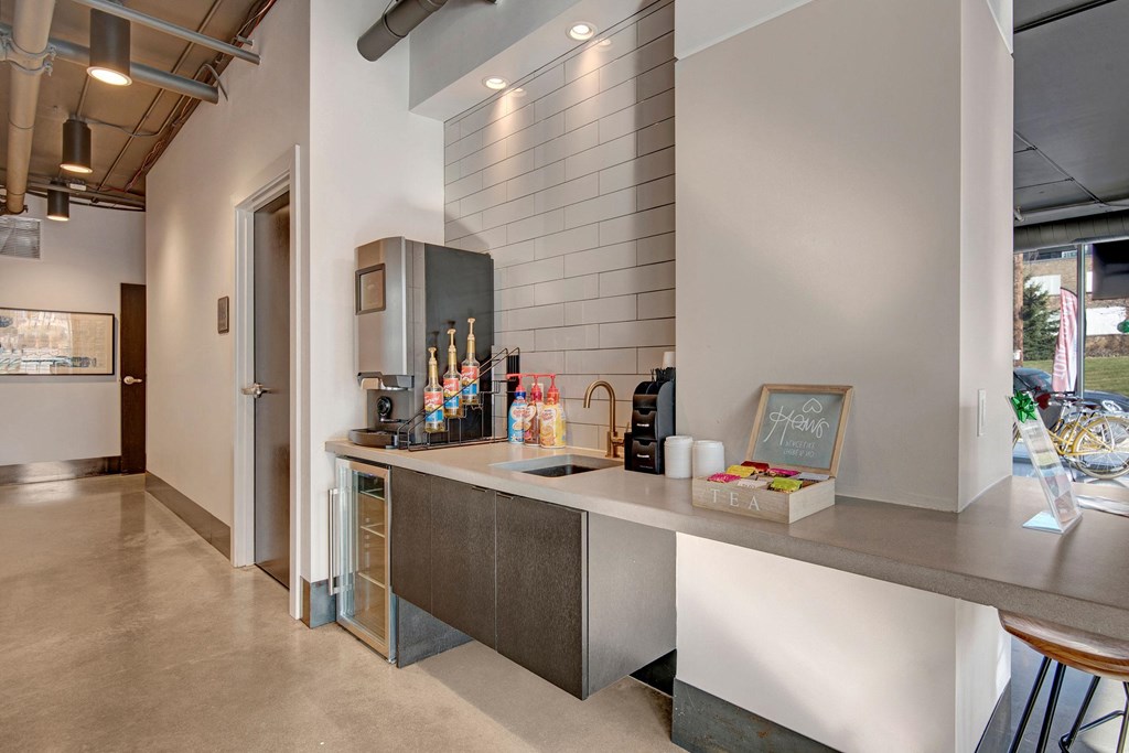 Modern coffee station with a sleek countertop, drink dispensers, flavor syrups, and a tea selection at Stitchweld Apartments.