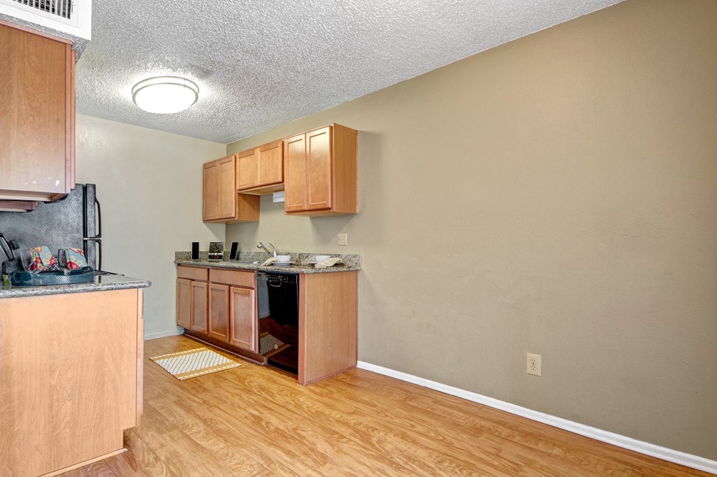 Cozy kitchen here at Avalon Springs Apartment Homes with wooden cabinets, black appliances, granite countertops, and light wood flooring. A bright ceiling light creates a warm, inviting space.