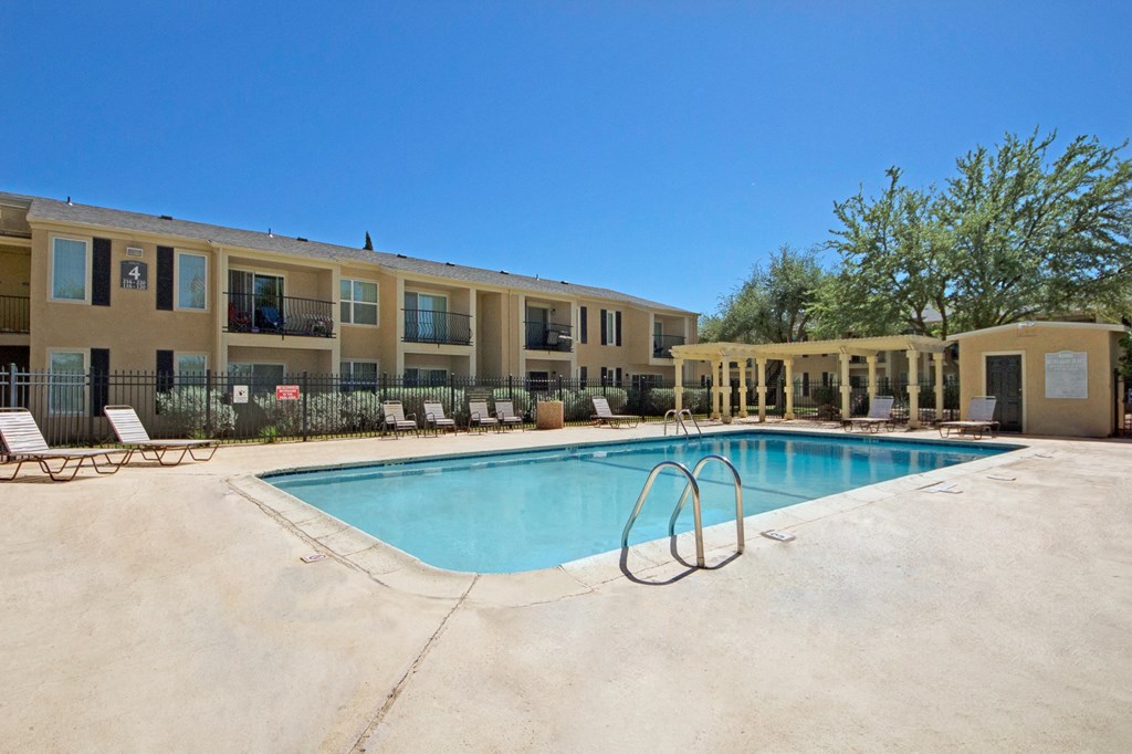 Avalon Springs Apartment Homes complex with a rectangular pool, surrounded by tan lounge chairs and trees, under a clear blue sky. The mood is serene and inviting.