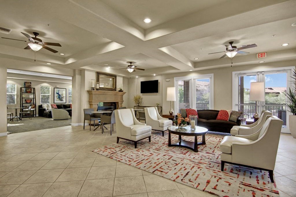 Elegant resident lounge here at Bela Rosa Apartments with tiled floor, cozy seating, and a patterned rug. Natural light streams through large windows, creating a welcoming ambiance.