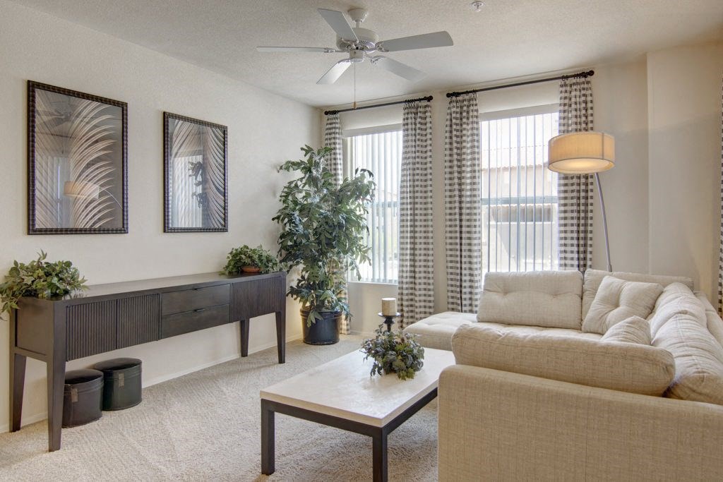 Neutral-toned living room here at Bela Rosa Apartments with a cozy sectional sofa, coffee table, and floor plant. Two framed artworks hang above a console table with decor.