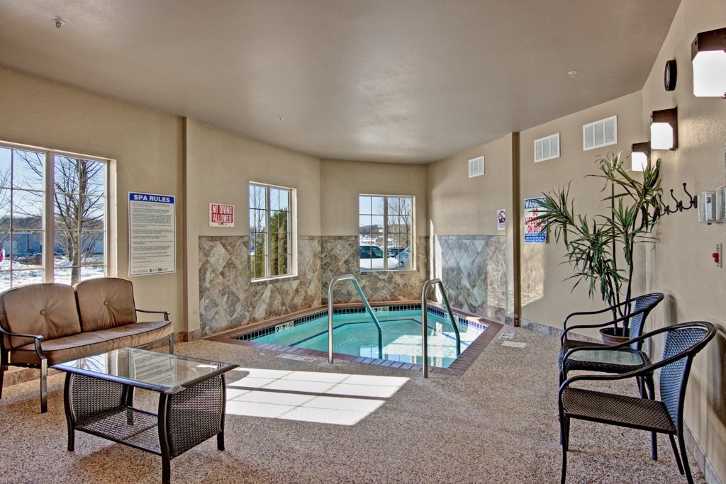 Cozy indoor spa room here at Grand River Estates Apartment Homes with a small pool, surrounded by four windows. There are chairs, a glass-top table, plant, and a warm, inviting atmosphere.