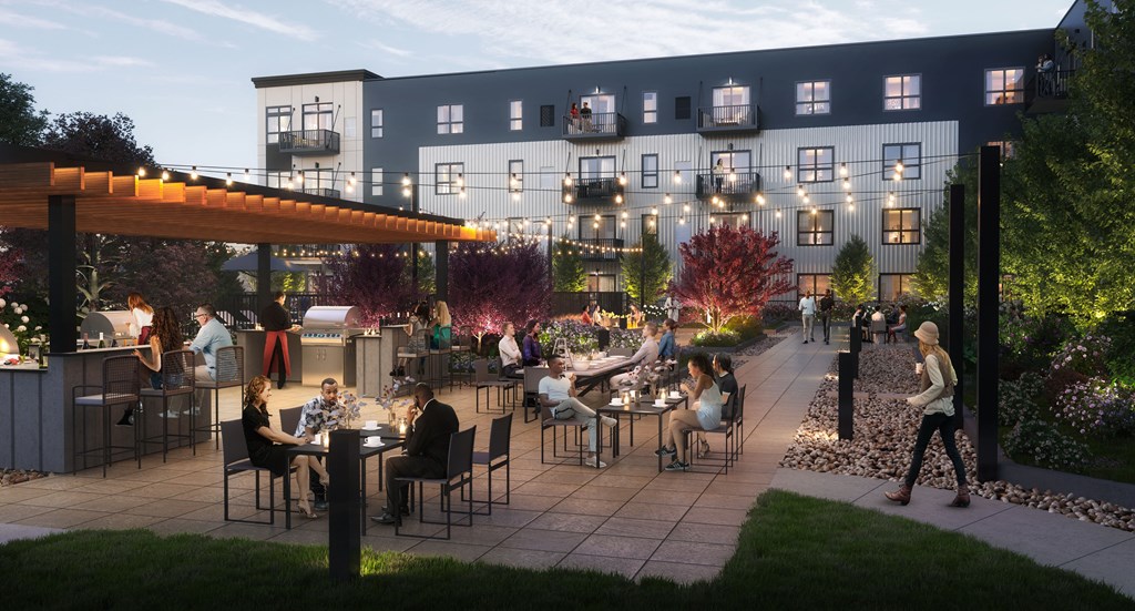 A lively outdoor gathering at the modern The Collection at Highland Bridge Apartment Homes complex. People seated under string lights enjoy food and drinks. Trees and flowers create a cozy atmosphere.