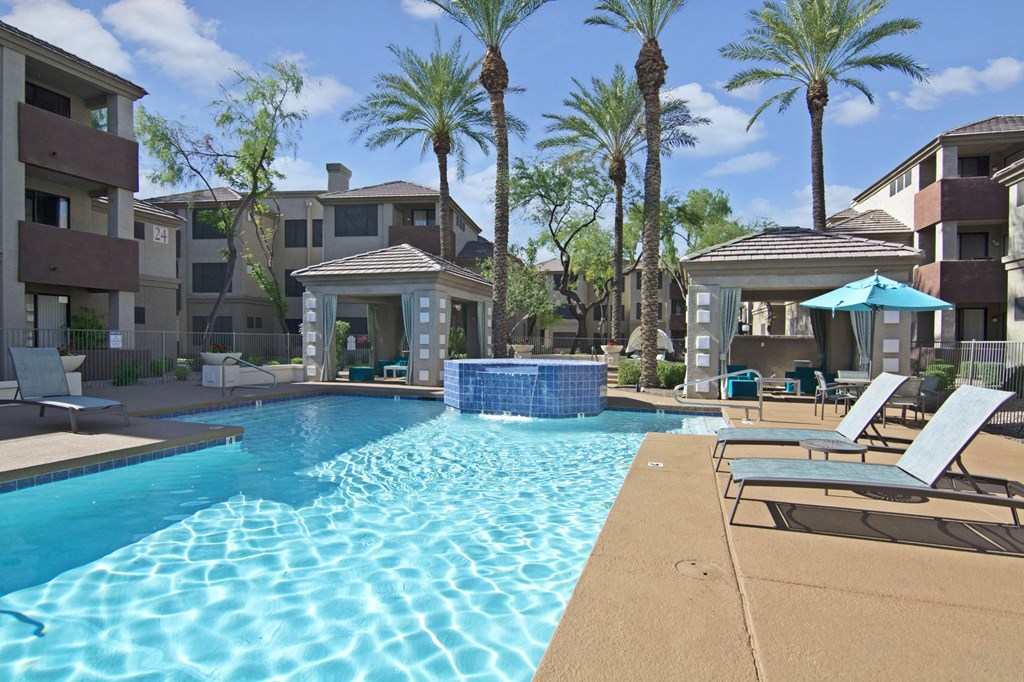 a swimming pool with lounge chairs and umbrellas with apartment buildings in the background
