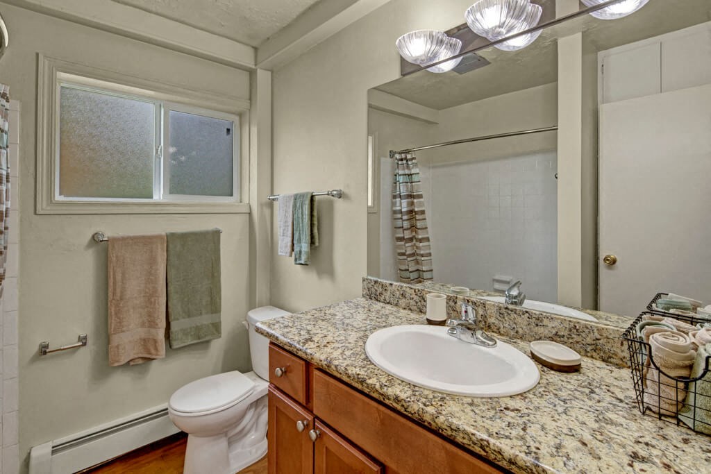 A modern bathroom here at Montclair Apartments with a granite countertop and sink, adjacent to a toilet. Towels hang by a frosted window, and soft, warm lighting creates a cozy ambiance.