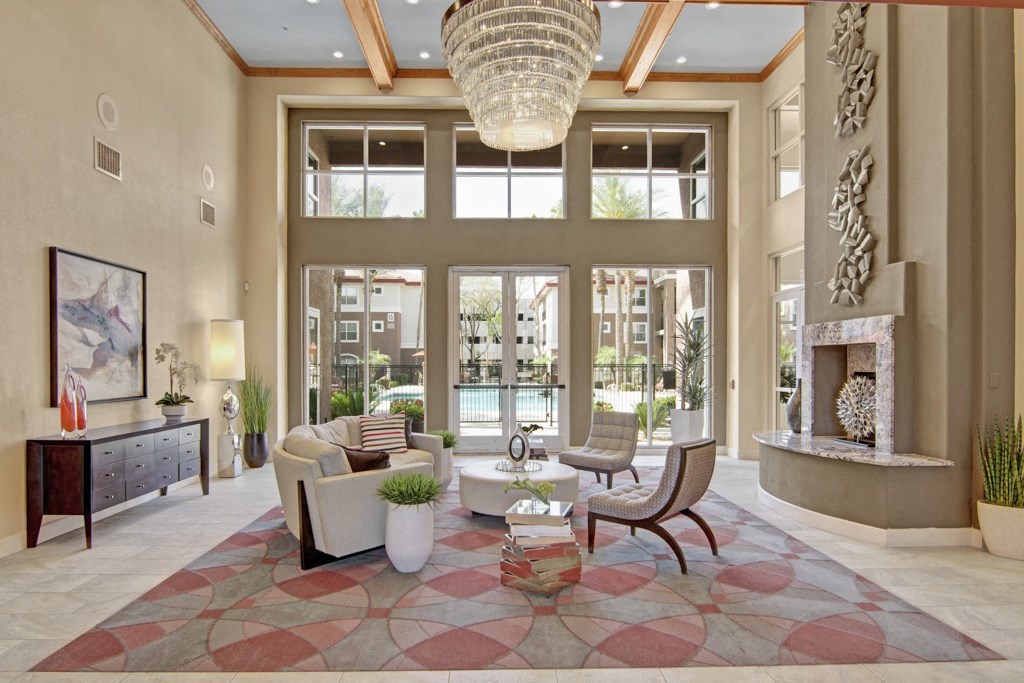 Luxurious resident lounge here at Mozaic at Steele Park Apartments with a high ceiling and large windows showcasing a pool view. Features modern furniture, abstract art, and an elegant chandelier.