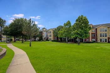 a grassy area with trees and apartment buildings in the background