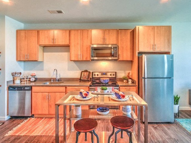 A cozy kitchen with wooden cabinets, a stainless steel fridge, microwave, and a small dining table set for two at Stitchweld Apartments.
