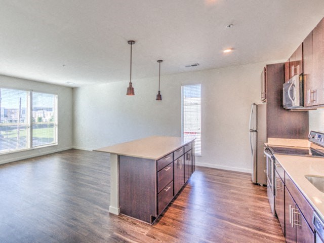 Spacious, modern kitchen with hardwood floors, a large island, pendant lights, and bright natural light at Stitchweld Apartments.