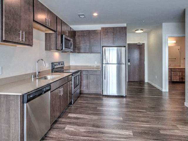 Modern kitchen with brown cabinets, stainless steel appliances, and hardwood floors at Stitchweld Apartments.