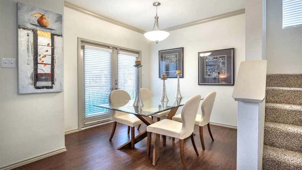 Elegant dining room here at Lakewood on the Trail Apartment Homes with a glass table and six cream chairs. Modern art decorates the walls. A warm, inviting atmosphere with natural light.