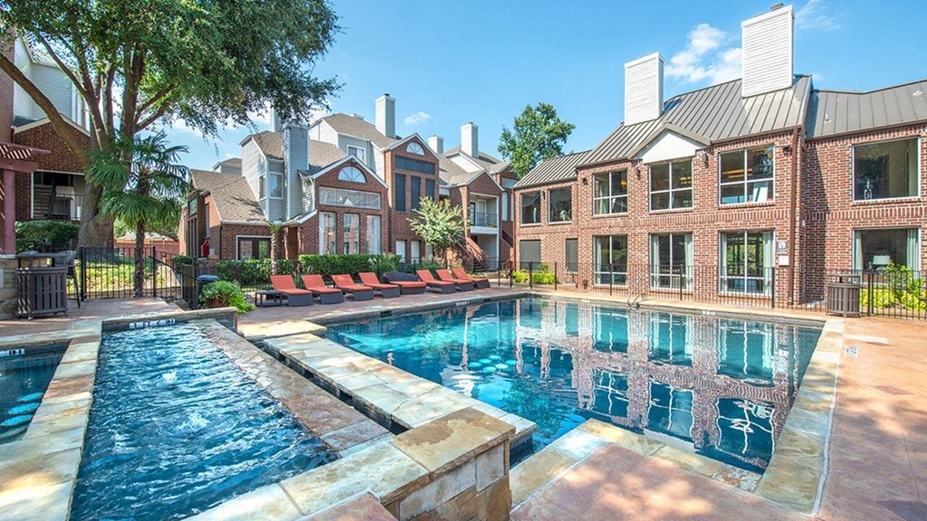 Swimming pool here at Lakewood on the Trail Apartment Homes with calm blue water, surrounded by brick buildings and green trees. Lounge chairs line the deck, creating a relaxing atmosphere.