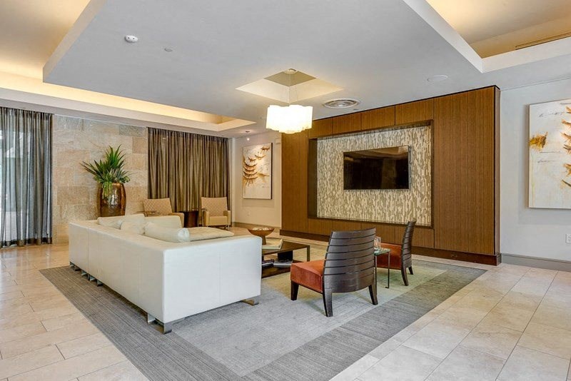 Modern living room here at Cityplace Heights Apartment Homes with a white sofa, two brown chairs, and a large wooden wall with a TV. Decor includes abstract art and a large plant, creating a calm, elegant ambiance.