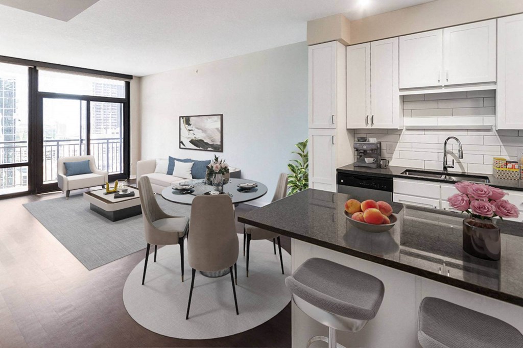 Modern open-concept living and kitchen area here at Nic on 5th Apartment Homes with large windows. Features white cabinets, a round dining table, and a cozy seating area with soft tones.